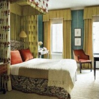 Elegant bedroom interior with patterned drapery, a neatly made bed, matching armchair, and a small desk area.