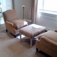 A well-lit room with an armchair and matching ottoman, alongside a side table with a lamp.