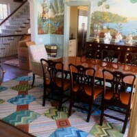 Elegant dining room with a wooden table and chairs, colorful geometric rug, and a mural on the wall, mid-move with a cardboard box present.
