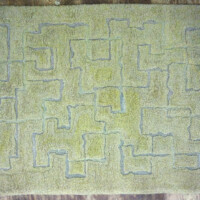 A worn, patterned rug with maze-like design on a floor.