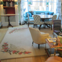 A cozy, well-lit room featuring eclectic furniture, decorative rug, and a view of the outdoors through windows with blue curtains.