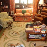 A cozy home library with overstuffed chairs and stacks of books on the floor.