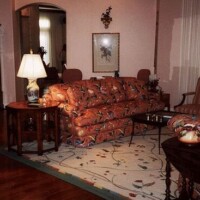 A vintage-style living room with floral-patterned sofas, a wooden coffee table, a traditional lamp, and decorative items.