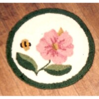 A handcrafted rug with a pink flower and a small bee design on a wooden floor.