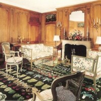 Traditional sitting room with wooden paneling, floral upholstered furniture, and a patterned rug.