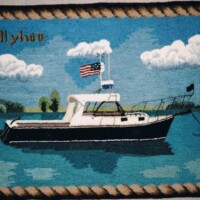 Embroidered depiction of a boat named "ballyhoo" with an american flag, floating on water with clouds in the background.