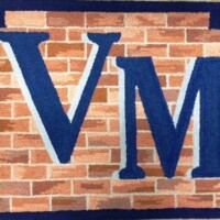 Embroidered letters "vm" against a brick-patterned background on fabric.