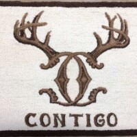 Embroidered badge with a stylized deer antler design and the word "contigo" below it.