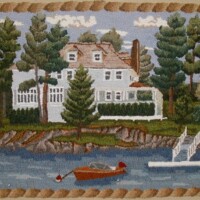 Embroidered scene of a white house with trees by a lake with a small boat and dock.