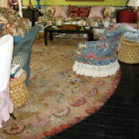 An eclectic living room with patterned upholstery, a floral rug, and dark wooden floors.