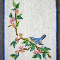 Embroidered image of a bluebird perched on a branch with pink blossoms.