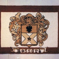 Embroidered family crest with heraldic symbols on a brown background.
