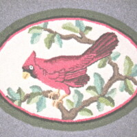 Oval-shaped rug featuring a red bird perched on a branch with green leaves, bordered by a dark green edge.