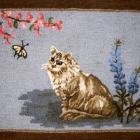 A latch hook rug depicting a cat watching a butterfly among flowers.