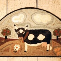 Semi-circular rug with a folk art design featuring a cow, trees, and clouds.