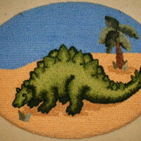 Latch hook rug depicting a green stegosaurus with a desert and blue sky background.