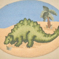 Embroidered depiction of a green stegosaurus with a blue sky and desert landscape.