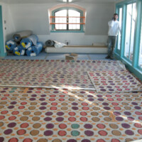 A man stands in a room with colorful patterned carpet during what appears to be a renovation or construction process.