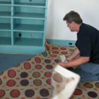 Man kneeling on a patterned carpet rolling up a section of the carpet.