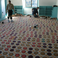 Two workers installing carpet with circular patterns in a room.