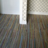 A room corner with striped carpet and patterned wallpaper.