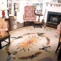 A traditional living room with a floral armchair, fireplace, and an ornate bird-themed area rug.