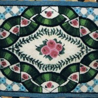 Handcrafted floral rug with symmetrical pattern and pink, green, and blue hues displayed on a wall.