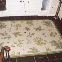 A hand hooked white entrance rug with green fern and butterflies by GW Ruggery.