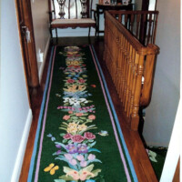 A narrow hallway featuring a floral runner rug, wood railings, and a decorative table at the end.