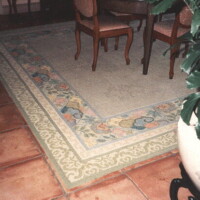 Area rug with floral border pattern in a room with terracotta tiles and furniture.