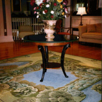 An ornate flower arrangement on a black-legged table in a living room setting.