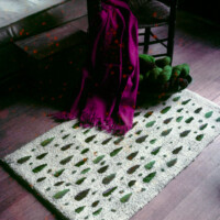 A colorful scarf draped over a rustic wooden chair with a textured rug below, displaying a pattern of green leaves.