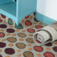 Patterned area rug partially rolled up near a turquoise table leg on a hardwood floor.