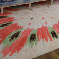 A patterned rug with green, red, and brown abstract designs on a pale background, partially under a piece of blue furniture.