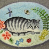 Embroidered image of a cat among flowers and insects on a fabric surface.