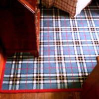 Plaid carpet in a room with wooden furniture and a red-bordered matching rug.