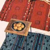 A vintage-style room featuring patterned red and blue rugs with a rattan side table holding a bowl of lemons.