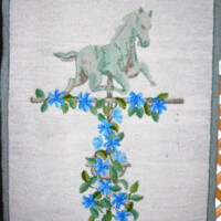 Embroidered tapestry featuring a horse atop a flowering vine, displayed within an octagonal frame.