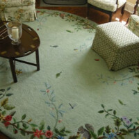 A cozy living room with a floral rug, featuring a wooden side table holding a glass of water and eyeglasses, next to an upholstered chair.